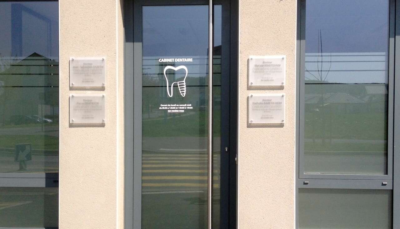 L'entrée du cabinet, avec les plaques des praticiens de part et d'autre de la porte vitrée